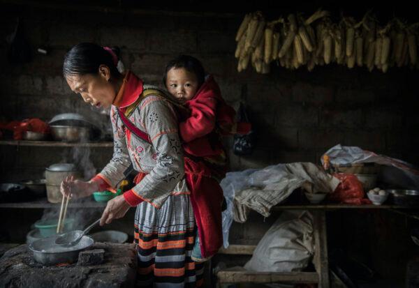 A woman of the Long Horn Miao ethnic minority group carries a baby on her back as she cooks in Xiaobatian village, Guizhou Province, China on Feb. 7, 2017. (Kevin Frayer/Getty Images)
