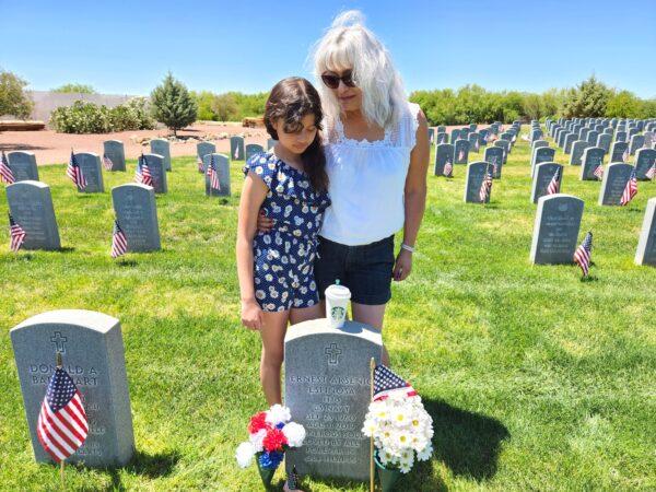 Diana Espinosa (R) and her granddaughter place a cup of black coffee on the gravestone of Diana's late husband, U.S. Navy veteran Ernest Arsenio Espinosa, who died Aug. 11, 2019. He was laid to rest with full military honors at the Arizona Veterans' Memorial Cemetery in Marana, Ariz. Photo taken on May 27, 2023. (Allan Stein/The Epoch Times)