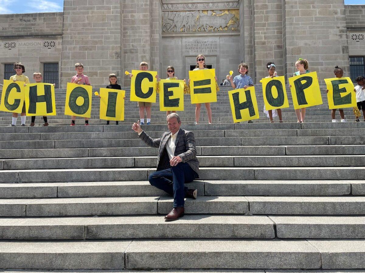 Nebraska Gov. Jim Pillen poses with children holding up signs promoting school choice at the state's capitol building on May 30, 2023. (Courtesy of the Nebraska Office of the Governor)