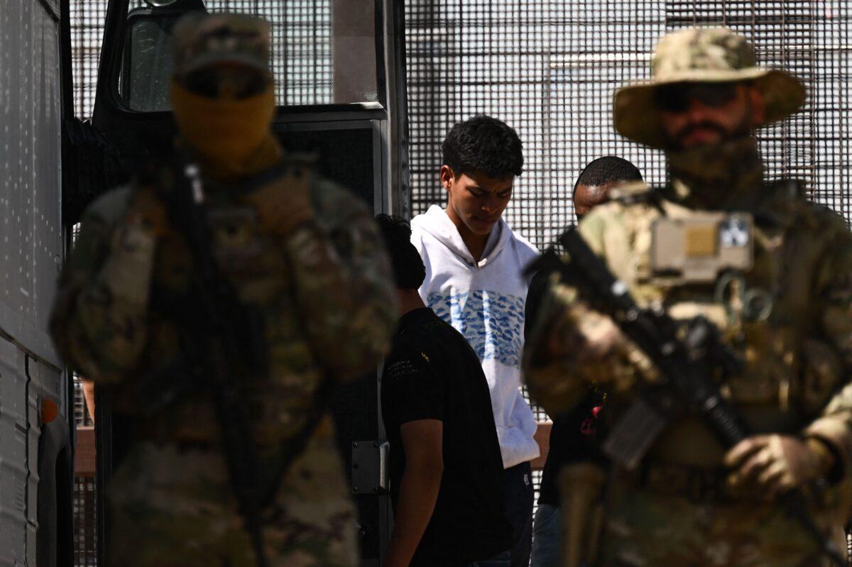 Texas Army National Guard look on as illegal immigrants board a bus after surrendering to U.S. Customs and Border Protection (CBP) Border Patrol agents for immigration and asylum claim processing following the end of Title 42 on the U.S.-Mexico border in El Paso, Texas, on May 12, 2023. (Patrick T. Fallon/AFP via Getty Images)