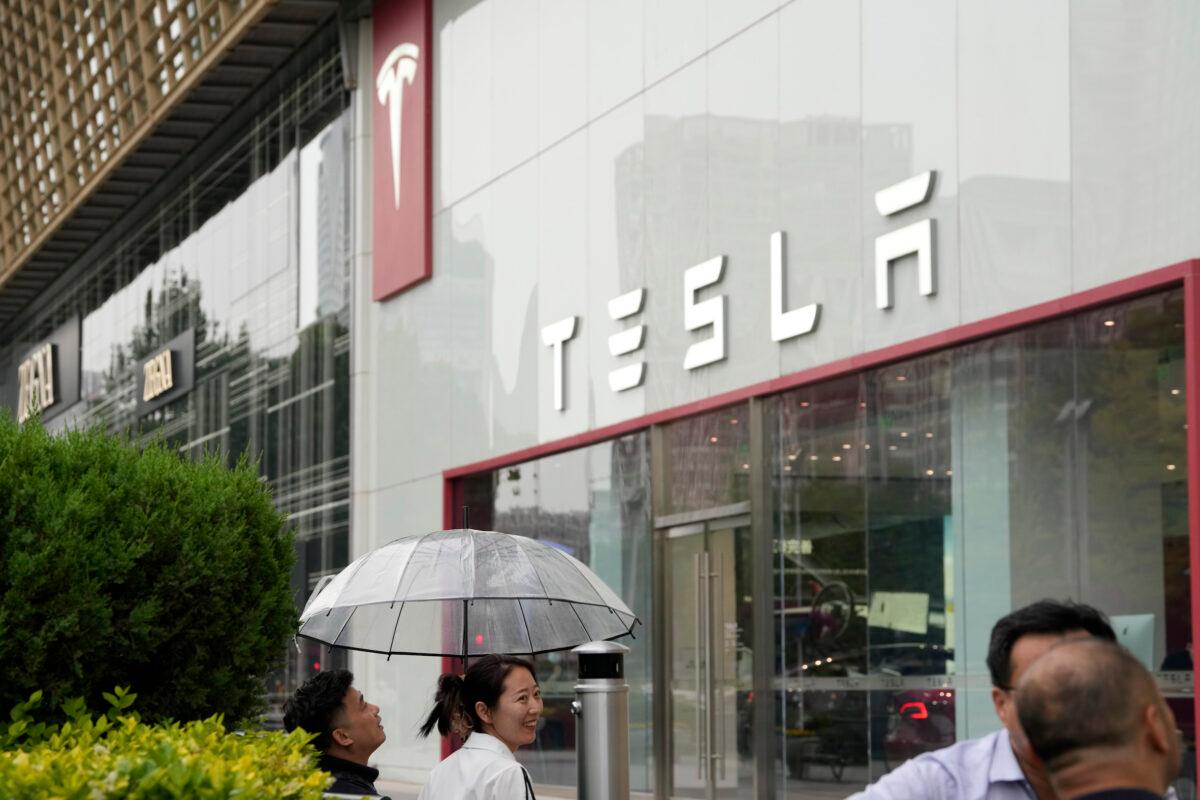 Workers chat under an umbrella outside the Tesla showroom in Beijing, China, on May 30, 2023. (Ng Han Guan/AP Photo)