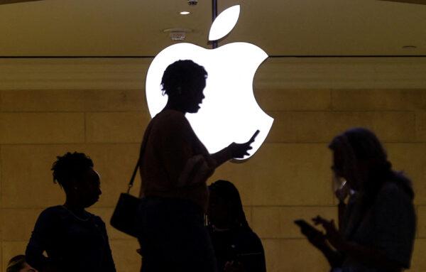 A woman uses an iPhone mobile device as she passes a lighted Apple logo at the Apple store at Grand Central Terminal in New York, on April 14, 2023. (Mike Segar/Reuters)