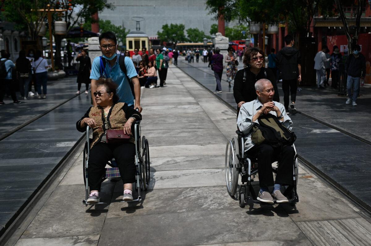 An elderly man and woman are pushed in wheelchairs along a street in Beijing on May 11, 2021. (Wang Zhao/AFP via Getty Images)