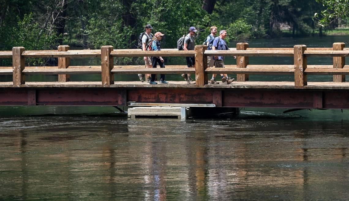 Yosemite National Park visitors cross the bridge which barely clears the water level on the Merced River at the Swinging Bridge picnic area in Yosemite Valley on Tuesday, June 14, 2023. (Craig Kohlruss/The Sacramento Bee/TNS)