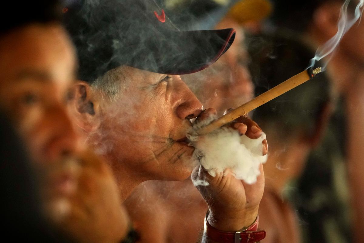 A Tembé Tenehara adult smokes and watches on as Indigenous adolescents perform the Wyra’whaw rite of passage in Brazil's Amazon rainforest. (Eraldo Peres/AP Photo)