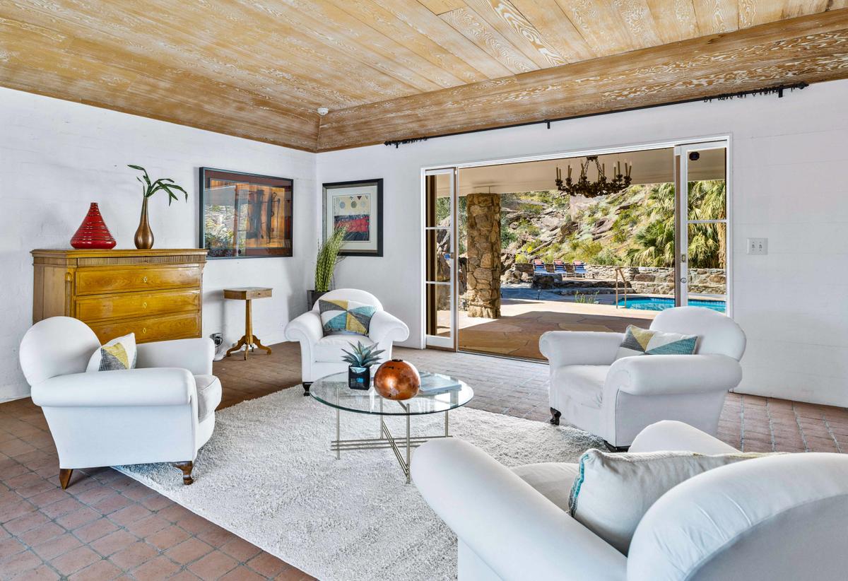 The spacious tiled living room has a ceiling accented by reclaimed wood, with glass walls that open onto a covered patio and the inviting pool beyond. (Courtesy of Kelly Peak, toptenrealestatedeals.com)