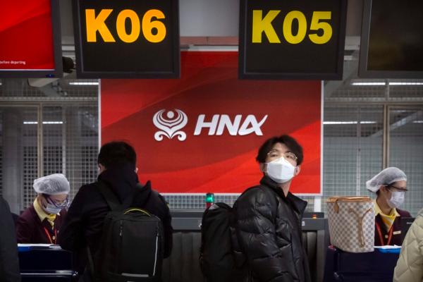 Travellers wearing face masks wait in line at the Hainan Airlines check-in counters at Beijing Capital International Airport in Beijing, on March 6, 2020. (AP Photo/Mark Schiefelbein)