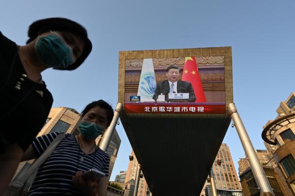 Two women wait below a giant screen showing news footage of China's President Xi Jinping speaking virtually at the Shanghai Cooperation Organization meeting, which was being held in India, at a shopping mall in Beijing on July 4, 2023. (Greg Baker/AFP via Getty Images)