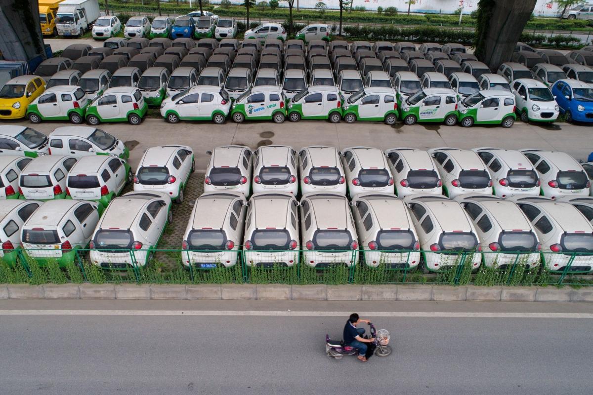 A motorist rides past new electric vehicles parked in a parking lot under a viaduct in Wuhan, in central China's Hubei province, on May 22, 2017. (STR/AFP via Getty Images)