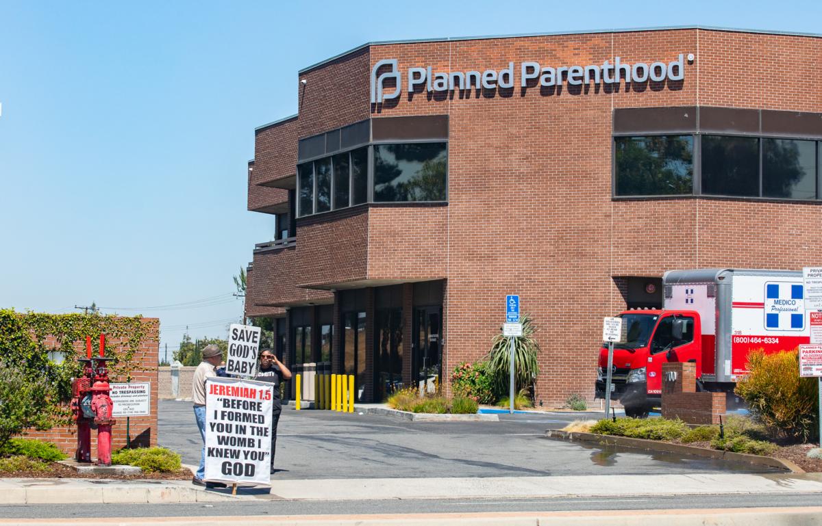 A Planned Parenthood security guard speaks with a man holding a sign in front of an organization facility in Orange, Calif., on June 28, 2022. (John Fredricks/The Epoch Times)