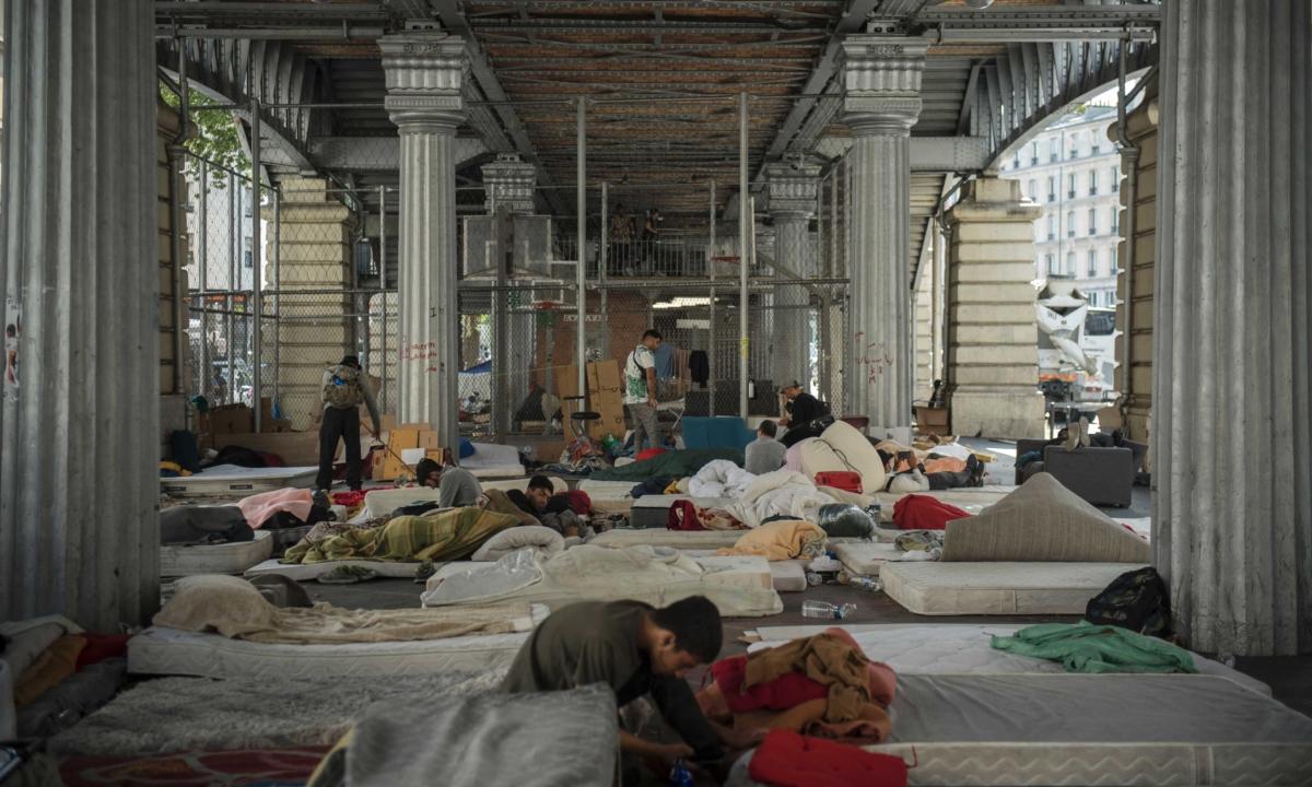 Men sit on their mattresses in the illegal immigrant camp in the Stalingrad district of Paris on July 12, 2023. (Julien De Rosa/AFP via Getty Images)