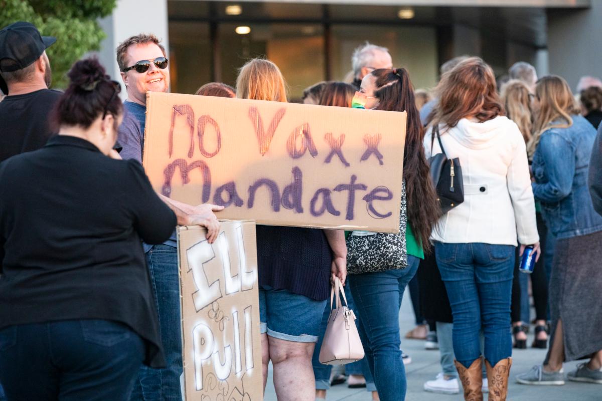 A waits in line while holding a sign with parents gathered to express their concerns over mandatory vaccine mandates for their children at the Placentia Yorba Linda Unified School District building in Placentia, Calif., on Oct. 12, 2021. (John Fredricks/The Epoch Times)