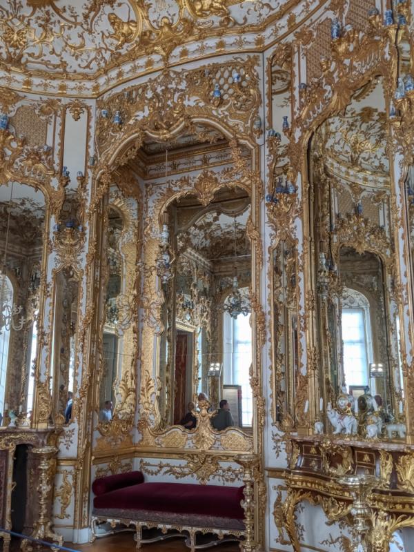 The Hall of Mirrors displays the playful Rococo style. As the name indicates, this room is covered with Rococo-style mirrors in ornate and complex frames, sculpted in plaster and gilded. The ceiling displays gilded floral and leaf motifs. A velvet bench, intricate inlaid wood cabinet, and delicate porcelain figures decorate the room. (Andrus Ciprian/Shutterstock)