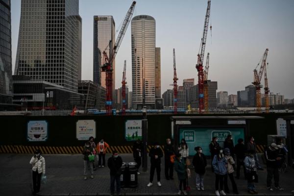 People wait for buses at a bus stop near a construction site at the central business district in Beijing on March 26, 2023. (Jade Gao/AFP via Getty Images)