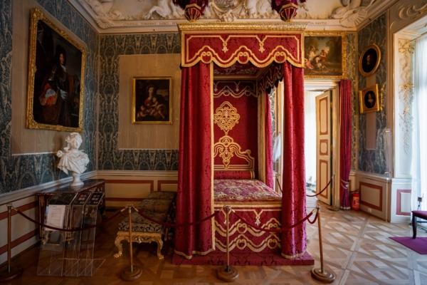 Genoa-style velvet wallpaper hangs in the king’s bedroom. The art and decorative work throughout the room reflect allegories of summer, such as the painting above the door frame (and the queen’s bedroom reflects springtime scenes). Eighteenth-century French furniture fills the room, including Louis XIV stools and a copy of a chest of drawers made in the workshop of preeminent French cabinetmaker André-Charles Boulle for Louis XIV’s chief minister, Cardinal Mazarin. (<a href="https://www.shutterstock.com/image-photo/warsaw-poland-aug-26-2019-kings-2113229354">Diego Grandi</a>/Shutterstock)