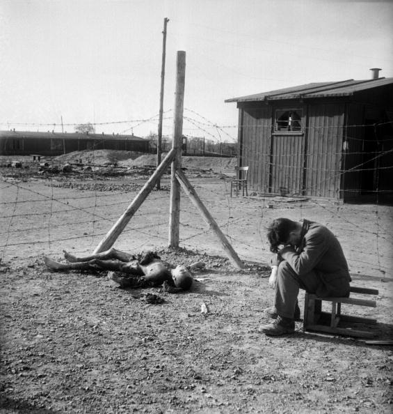 A young man sits on an overturned stool next to a burnt body in the Thekla camp outside Leipzig, Germany in April 1945, after the U.S. troops entered Leipzig. (Eric Schwab/AFP via Getty Images)