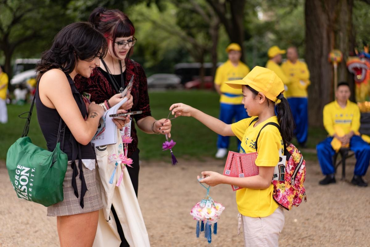 Passersby accept lotus flower decorations from a young Falun Gong practitioner on July 20. (Samira Bouaou/The Epoch Times)