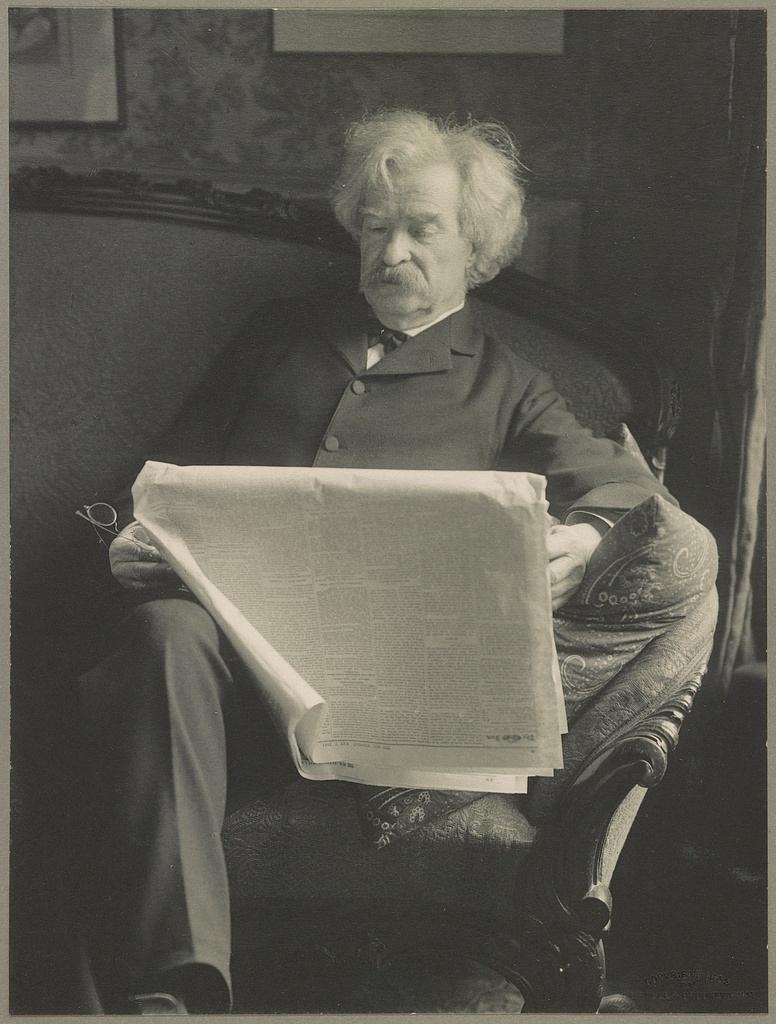 A photograph of Mark Twain, 1902, reading a newspaper. Library of Congress. (Public Domain)