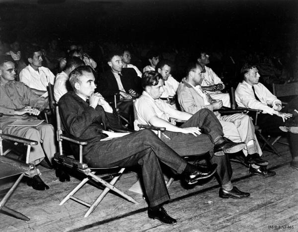A group of physicists at the 1946 Los Alamos colloquium on the Super. In the front row are Norris Bradbury, John Manley, Enrico Fermi and J.M.B. Kellogg. Behind Manley is Oppenheimer (wearing jacket and tie), and to his left is Richard Feynman. (Attributed to Los Alamos National Laboratory)