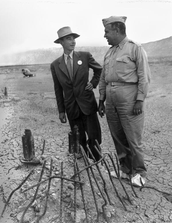 Oppenheimer (L) and Leslie Groves in September 1945 at the remains of the Trinity test in New Mexico. The white canvas overshoes prevented fallout from sticking to the soles of their shoes. U.S. Army Corps of Engineers. (Public Domain)