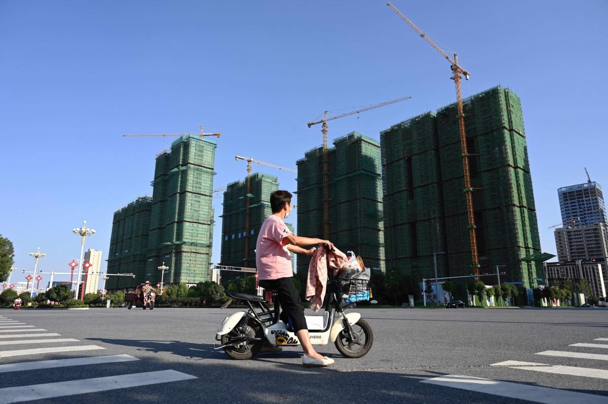 A woman rides a scooter past the construction site of an Evergrande housing complex in Zhumadian, Henan Province, China, on September 14, 2021. (Photo by JADE GAO / AFP) (Photo by JADE GAO/AFP via Getty Images)