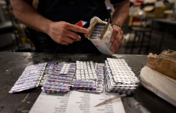 Election Offices Across US Get Voter Envelopes Laced With Fentanyl: Officials | USNN World News  An officer from the U.S. Customs and Border Protection, Trade and Cargo Division finds Oxycodone pills in a parcel at John F. Kennedy Airport's US Postal Service facility in New York on June 24, 2019. (Johannes Eisele/AFP via Getty Images)