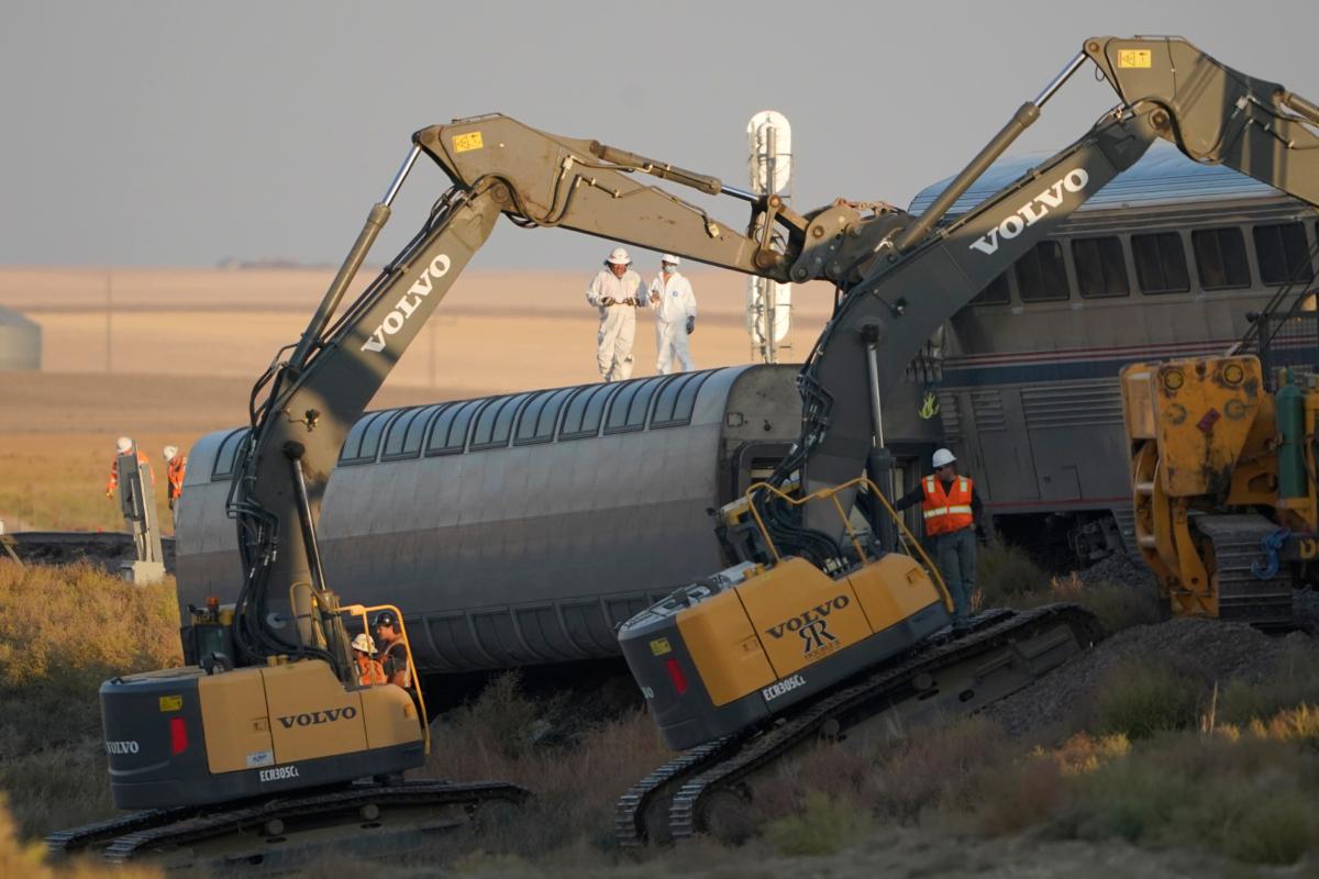 Workers stand on a train car on its side as front-loaders prop up another train car from an Amtrak train that derailed the day prior just west of Joplin, Mont., on Sept. 26, 2021. (Ted S. Warren/AP Photo)