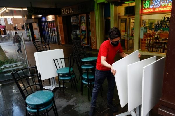 A woman sets up tables and chairs outside a restaurant in Melbourne, Australia, on July 28, 2021. (Con Chronis/AFP via Getty Images)