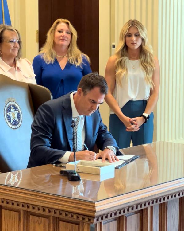 Oklahoma Gov. Kevin Stitt (seated) signs an executive order defining the biological sexes and ordering state offices to act according to those definitions on Aug. 1, 2023. Former collegiate swimmer and current women's rights activist Riley Gaines (right) looks on. (Courtesy of the Oklahoma Governor's Office)
