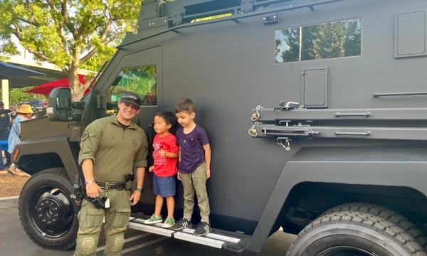 An Irvine SWAT officer poses for photo with local children alongside his unit’s SWAT truck at the city's National Night Out at Woodbury Community Park in Irvine, Calif., on Aug. 1. (Carol Cassis/The Epoch Times)