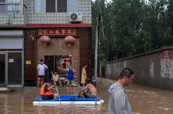Local residents, some in a makeshift boat, in front of their house in an area inundated with floodwaters near Zhuozhou, Hebei Province, China, on Aug. 3, 2023. (Kevin Frayer/Getty Images)