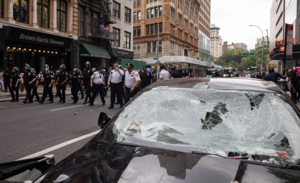 A shattered windshield is seen as police officers line up during riots sparked by Twitch streamer Kai Cenat, who announced a giveaway event in New York's Union Square on Aug. 4, 2023. (Yuki Iwamura/AFP via Getty Images)