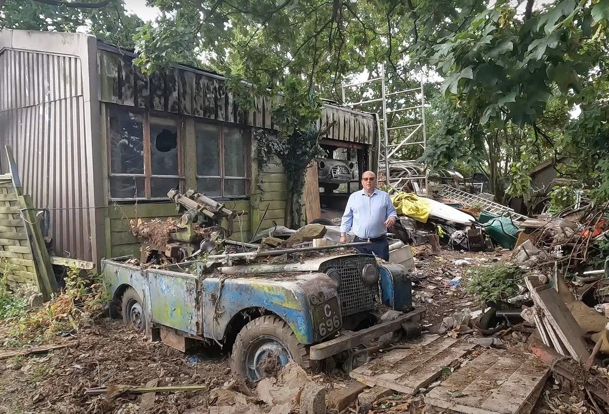 Guy Snelling from Anglia Car Auctions stands next to a beat-up 1951 Land Rover Series I at a decrepit barn on a property somewhere in the south of England. (Courtesy of Anglia Car Auctions)
