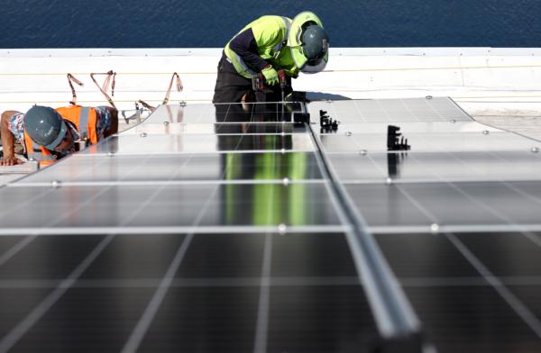 Workers install solar panels during the completion phase of a four-acre solar rooftop atop AltaSea's research and development facility at the Port of Los Angeles on April 21, 2023. (Mario Tama/Getty Images)