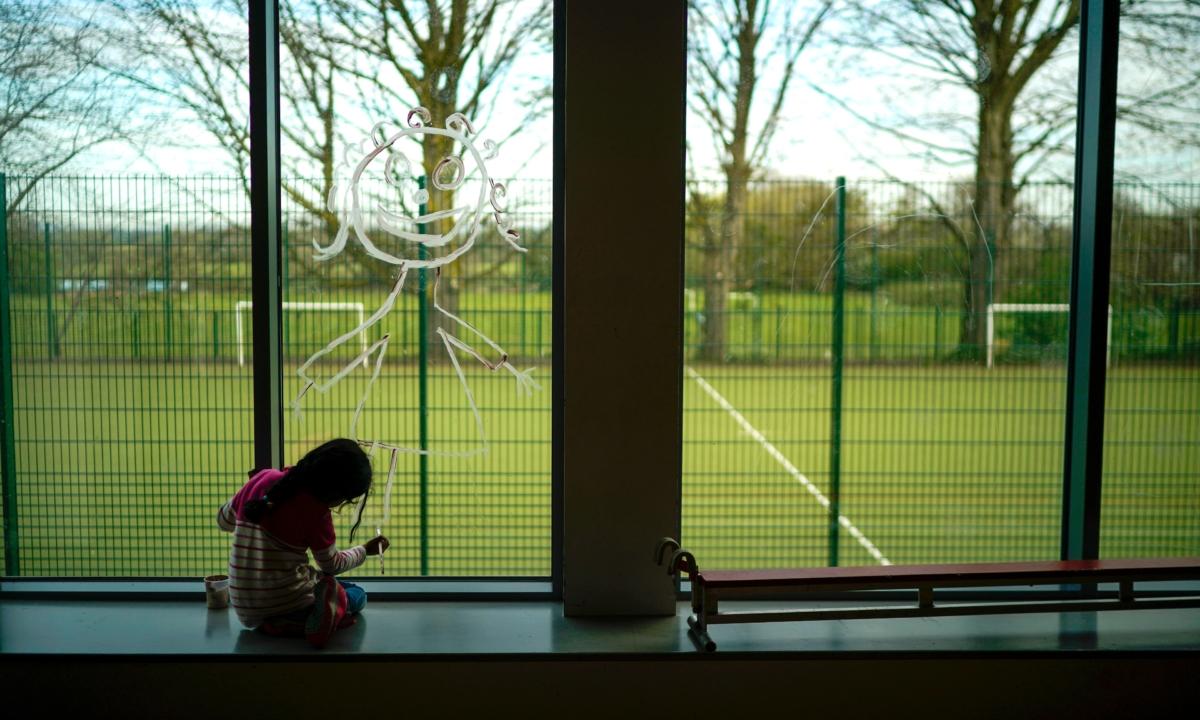A young girl paints a picture of herself on the school window as children of key workers take part in school activities at Oldfield Brow Primary School in Altrincham, England, during the first COVID-19 lockdown on April 8, 2020. (Christopher Furlong/Getty Images)