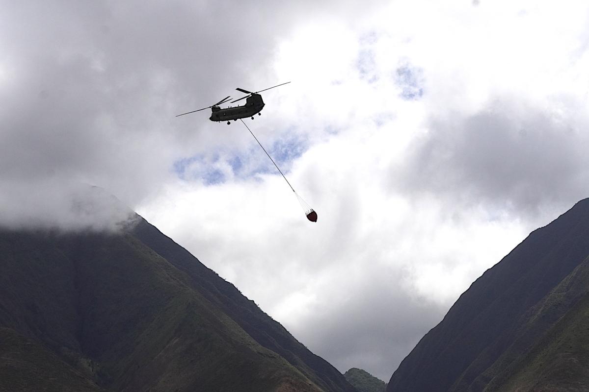 A military helicopter prepares to dump a bucket full of water on lingering hotspots from the Aug. 8 Lahaina wildfire disaster. Photo taken on Aug. 16, 2023. (Allan Stein/The Epoch Times)