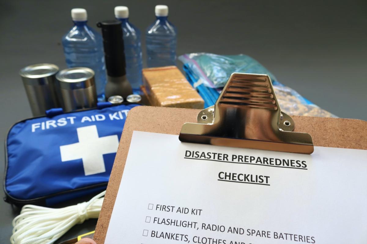 A disaster preparedness checklist, featuring a variety of disaster essentials, including a first aid kit, bottles of water, food, a flashlight, and extra batteries. (Speedshutter Photography/Shutterstock)