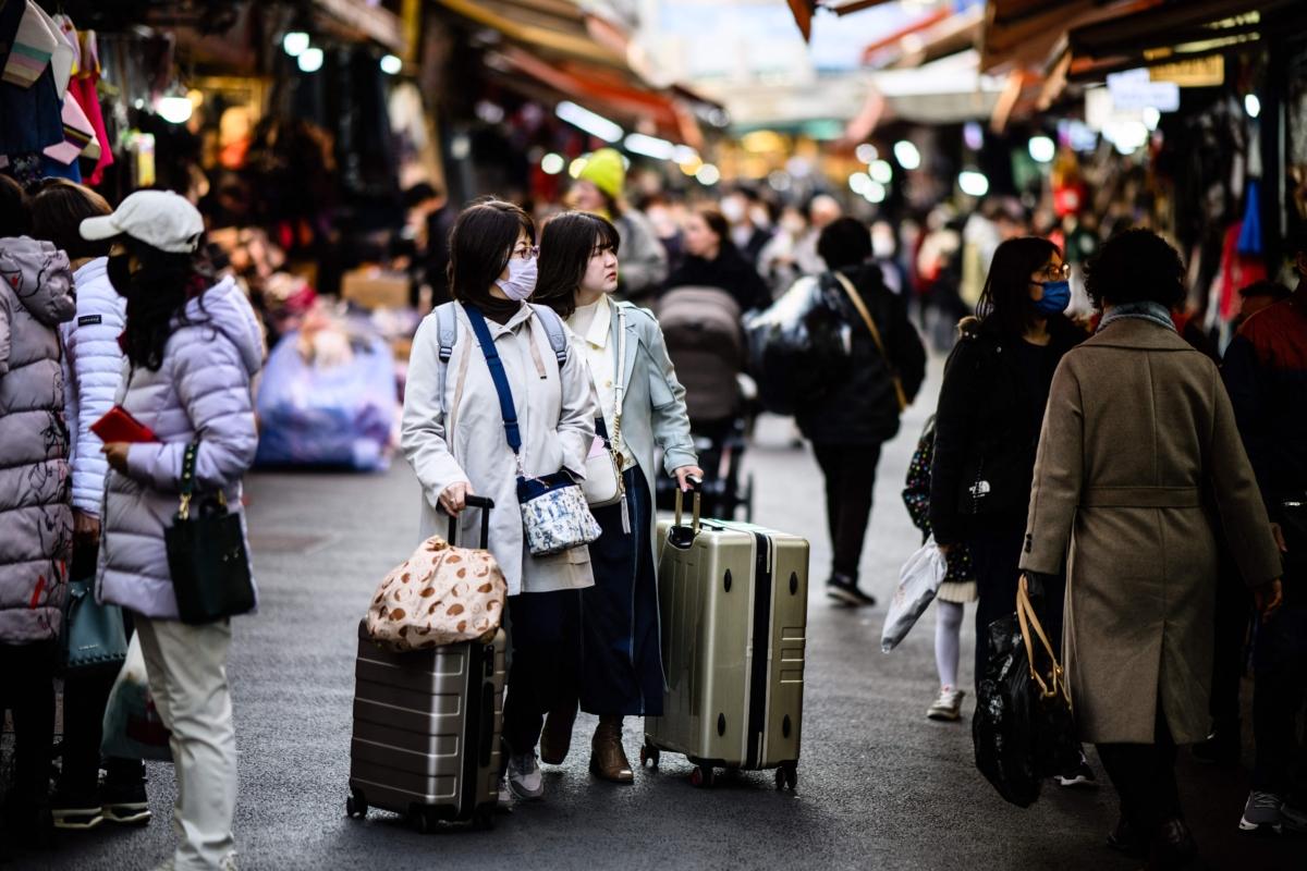 Tourists push their luggage past stalls as they visit Namdaemun Market in Seoul on March 13, 2023. (Anthony Wallace /AFP via Getty Images)