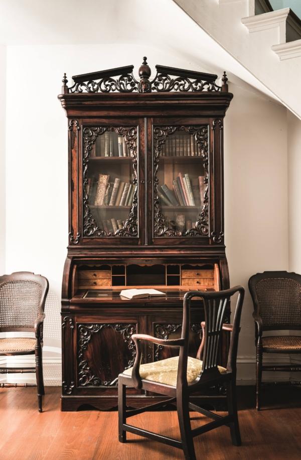 The 1840s Rococo Revival-style secretary in the mansion’s front parlor is original to the Nutt family, who had the residence built. Made of mahogany with a rosewood finish, the two-part roll-top desk has storage at the base and a glass-door bookshelf at the top. The Rococo Revival style is especially apparent in the sculpted wood moldings framing the glass doors at the top and the wooden doors below the desk. (Courtesy of Pilgrimage Garden Club)