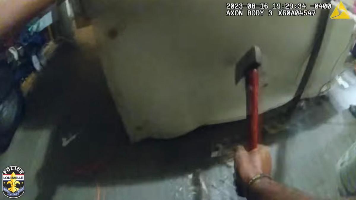 A screenshot of body camera footage shows an officer using a hatchet to cut the dog chain from the floor. (Courtesy of Louisville Metro Police Department)