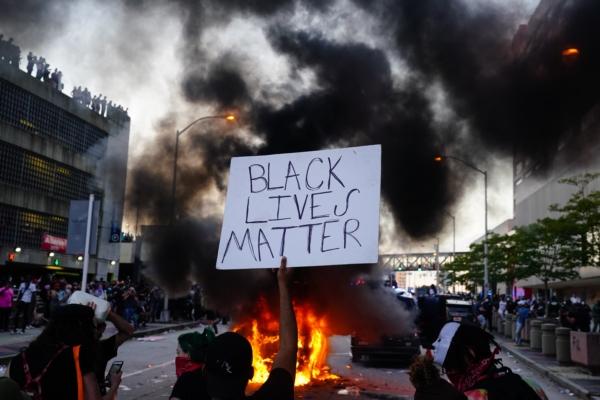 A man holds a Black Lives Matter sign as a police car burns in front of him during a protest over the death of George Floyd, outside CNN Center in Atlanta on May 29, 2020. (Elijah Nouvelage/Getty Images)