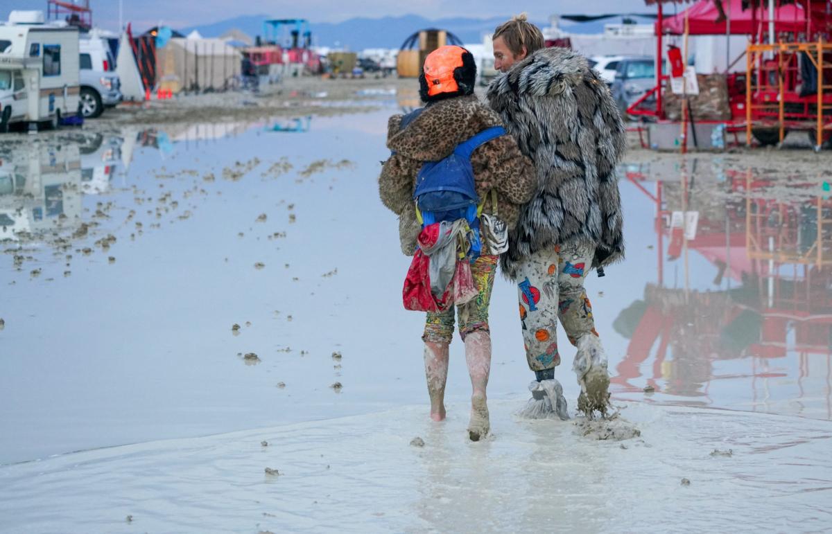 Dub Kitty and Ben Joos walk through the mud at Burning Man after a night of dancing with friends in Black Rock City in the Nevada desert on Sept. 2, 2023, after a rainstorm made the area impassable to vehicles. (Trevor Hughes/USA Today Network via Reuters)