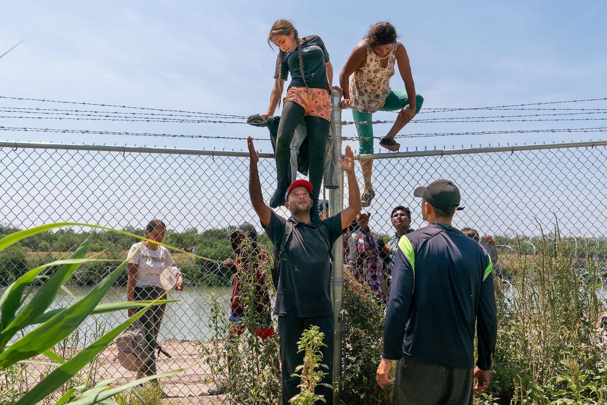 Illegal immigrants help each other climb over a barbed wire fence into the United States from Mexico, in Eagle Pass, Texas, on Aug. 25, 2023. (Suzanne Cordeiro/AFP via Getty Images)