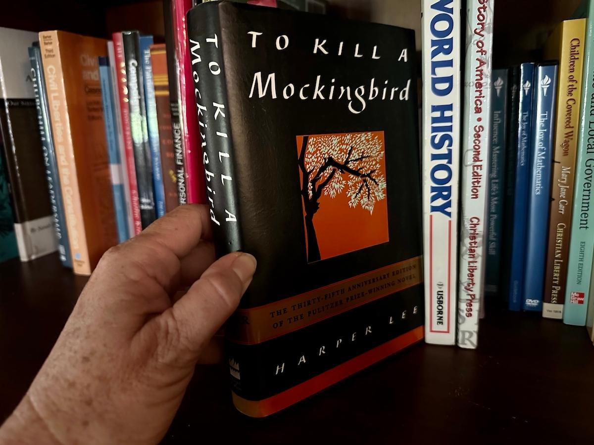 A homeschooling parent removes a copy of "To Kill a Mockingbird" from a bookshelf in Alachua, Fla., on Sept. 12, 2023. (Nanette Holt/The Epoch Times)