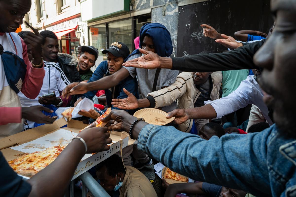 A police officer hands out pizza to dozens of recently arrived illegal immigrants to New York City as they camp outside of the Roosevelt Hotel, which has been made into a reception center, where they try to secure temporary housing on Aug. 1, 2023. (Spencer Platt/Getty Images)