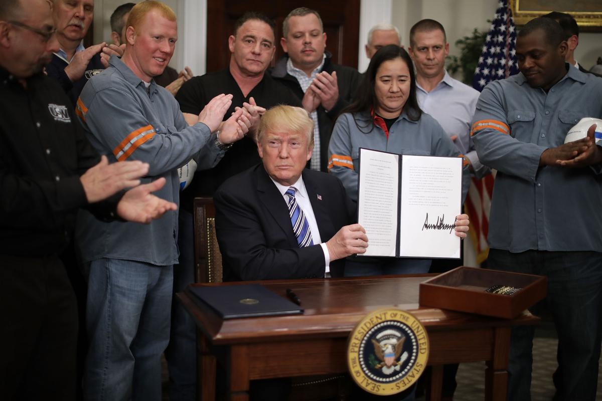 Surrounded by applauding steel and aluminum workers, U.S. President Donald Trump holds up the "Section 232 Proclamations" on steel imports, signed in the Roosevelt Room of the White House, on March 8, 2018. (Chip Somodevilla/Getty Images)