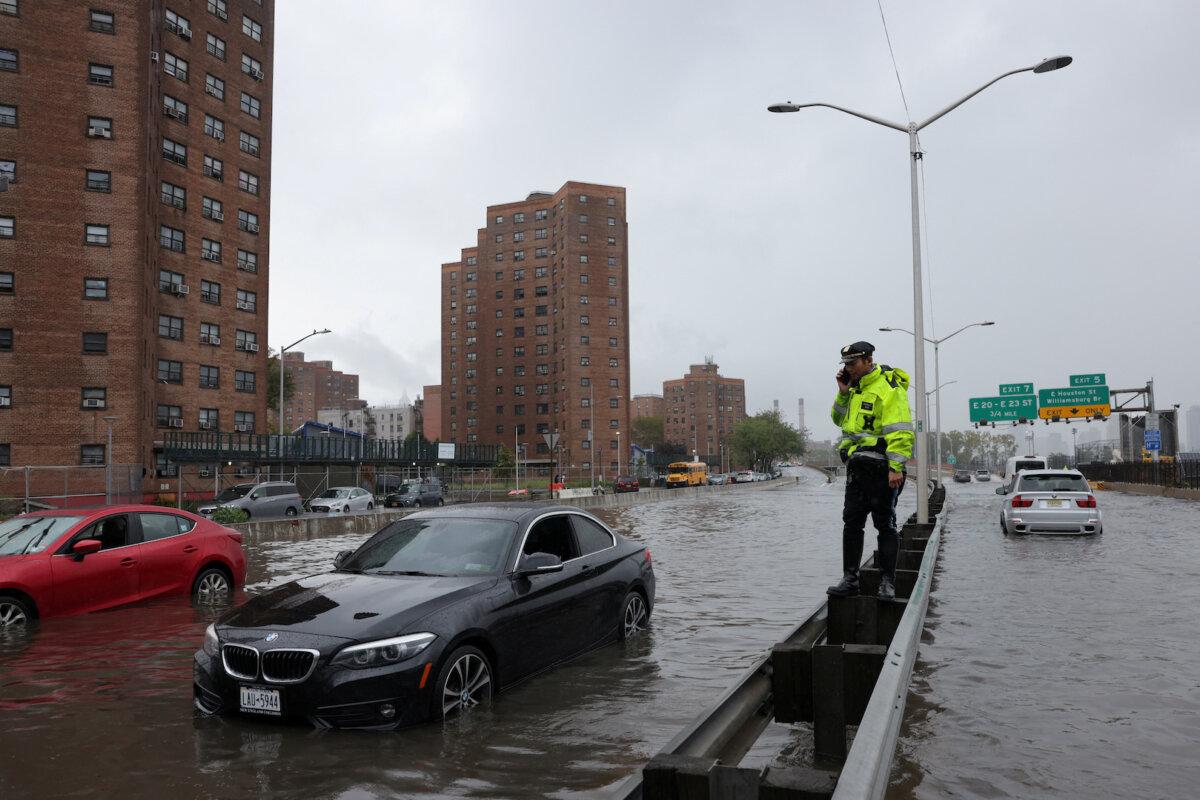 A police officer from the NYPD Highway Patrol uses his mobile phone next to cars stuck in a flooded street after heavy rains bring flooding across the mid-Atlantic and Northeast, at the FDR Drive in Manhattan near the Williamsburg Bridge, in New York City, on Sept. 29, 2023. (Andrew Kelly/Reuters)