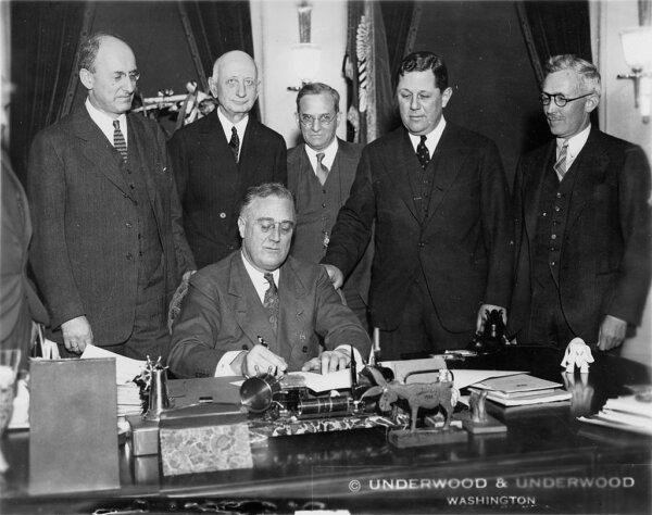 President Franklin Delano Roosevelt signs the Gold Reserve Act into law in 1934. Standing behind him are (L-R) Henry Morgenthau Jr. (Treasury secretary), Eugene R. Black (Fed chair), George Warren (economist and advisor), Samuel Rosman and James Harvey Rogers (economist and advisor). (Public Domain)