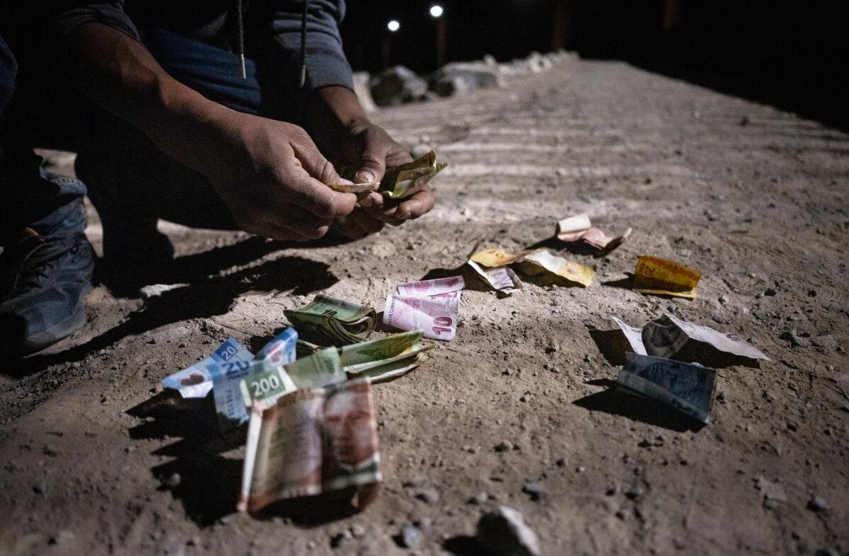 A man collects discarded identification and currency abandoned by illegal immigrants before crossing into the United States, in northern Mexico on May 18, 2023. (John Fredricks/The Epoch Times)