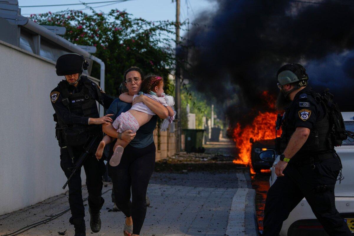 Police officers evacuate a woman and a child from a site hit by a rocket fired from the Gaza Strip, in Ashkelon, southern Israel, Saturday, Oct. 7, 2023. (AP Photo/Tsafrir Abayov)